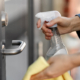 Close up of hands cleaning outdoor door handle surface with detergent spray