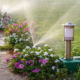 Plastic sprinkler irrigating flower bed on grass lawn with water in summer garden